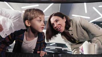 Close-up view from the trunk of a car a little blond boy with blue eyes in a checkered shirt looks into the trunk of a modern car in a car showroom with his parents video