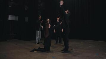 A group of confident actors in black suits of young theater university students are rehearsing showing expression during actions along with their young male stage director with papers in their hands video