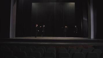 Side view of a group of confident and happy actors in black clothes in the theater going on stage near a black curtain during a rehearsal in an empty hall video