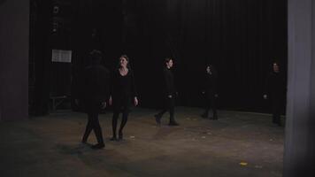 A group of confident young actors in black clothes enter the stage near a black curtain and at the same time stop practicing theatrical movement and freezing in place at a theater university video