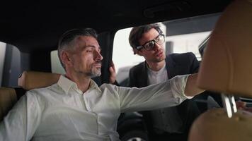 A confident middle-aged man with gray hair in a white shirt inspects the inside of a car before purchasing while communicating with the manager a guy in a business suit in a car showroom video