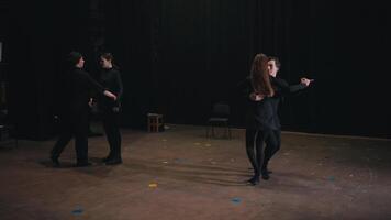 Two pairs of confident actors in black suits dance on stage during their rehearsal for a play in the theater. Careful preparation of actors in black suits before performing and dancing in the theater video