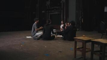 A group of happy young actors in black uniforms together with their director analyze and discuss the stages of the script and the roles of the actors before preparing for the performance on stage in video
