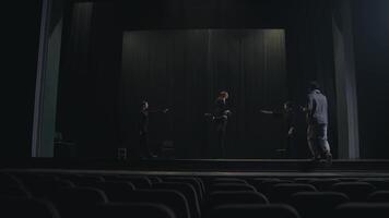 View from the audience two confident actors play the final scene with their stage director in a gray T-shirt and scarf during their rehearsal on stage in an empty theater with black curtains video
