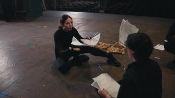 Zoom in confident and expressive brunette girl actor in a black suit sits on stage in the theater and talks with another actor about his role and script video