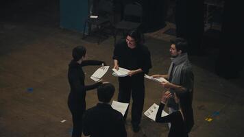 Top view of a group of confident actors in black suits Standing in a circle and talking to each other holding sheets of paper with a script in their hands and talking together with their director video