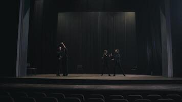 Two pairs of active actors in black suits dance their slow dance on stage during preparation for a performance and rehearsal in an empty theater video