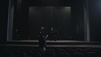 Rear view of a young male production director standing in the hall and showing how to move the actors and what to do on stage during a rehearsal in an empty theater with black curtains video