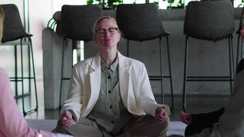 A group of confident businesswomen in business clothes meditate while sitting on the carpet during their break between work in a modern office video