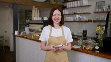 Portrait of a happy brunette girl waitress in a yellow apron who holds a notepad in her hands for writing down orders in a cafe video