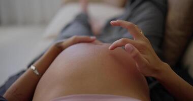 Top view close up of happy pregnant woman stroking her belly with fingers and gentle touches while lying on sofa at home video