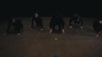 Five confident theatergoers actors stand in a row in black theater clothes and practice synchronized movement during their preparation and rehearsal in the theater on stage near black curtains video