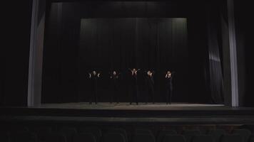 A group of actors in black stage clothes in the theater perform synchronously and practice synchronized movement in on stage in the theater near black curtains video
