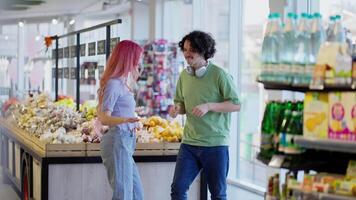 ein glücklich Mädchen mit Rosa Haar im Jeans und ein Brünette Kerl im ein Grün T-Shirt sind Tanzen in der Nähe von das Zähler im ein Supermarkt während ihr Einkaufen video