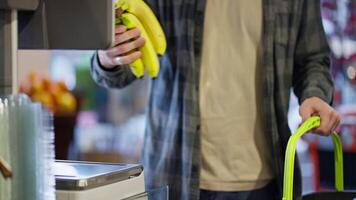Close up Supermarket visitor weighs bananas using scales in supermarket. A guy in a plaid shirt uses a scale to weigh bananas while shopping in a supermarket video