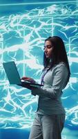 Vertical Software developer solving tasks on laptop, running artificial intelligence programming scripts. Woman using notebook to write lines of code for AI applications development, camera B video