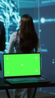 Vertical Teamworking AI technicians using green screen laptop for business data analysis. Team of IT experts works on mockup notebook to automatize tasks using artificial intelligence, camera A video