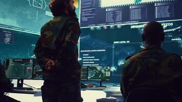 Colonel overseeing special operation to gather intelligence in control center with CCTV surveillance information on a big screen. Specialist targeting enemy military power base. Camera B. video