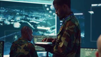 Military sergeant targeting enemy vessels on a gps satellite world map, operating from army power base monitoring room. Officer studies defense tactics on a tablet, command center. Camera A. video