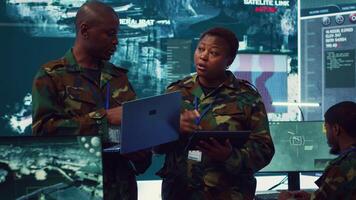 Sergeant major and female soldier checking real time field data in command post monitoring room, examining missions and operations. Team of troops interprets satellite imagery. Camera A. video