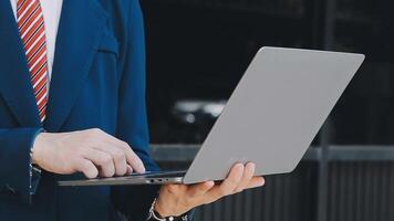 Handsome young executive standing in front of corporate building, holding tablet and smiling video