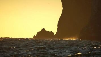 Red burning sunset, with a cliff in the background. The golden warm waters and its small wave ripples, along with bokeh lights from the sun. Abstract nature summer ocean sea. video
