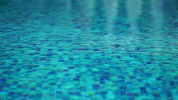 Pool water background with wavy clear fresh water. Calm rest on sunny day. Abstract reflections on the surface of the water with texture of bright blue pool tiles. Turquoise water surface. Slow motion video