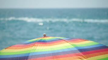 Rainbow colored beach umbrellas or parasols against blue sea during a sunny day on a beach. Symbol of vacations, relax, summer. Colorful umbrellas from the sun stand on the beach. Slow motion. video