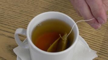 Steeped Tea Bag in a White Mug. A white mug filled with tea with lemon slice and a tea bag with a string being pulled out. video