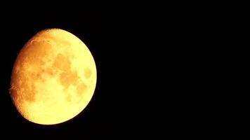 Timelapse. A glowing golden huge moon as seen from earth through the atmosphere against a starry night sky. A large moon moves across the sky, the moon moving from the left frame to the right. video