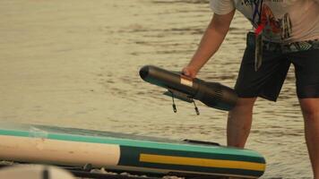 Man take off Motor for Paddleboard, A man in shorts holds a motor for a paddleboard in a shallow body of water. video