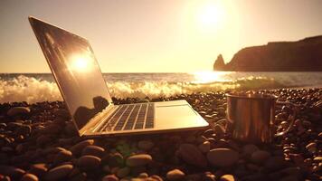 Silhouette of laptop and cup on the beach over sea sunset. Sparkling sea water on background. Freelancer, blogger working on notebook on the beach. video