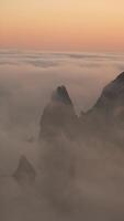 Misty Sunset Over Rugged Cliffs. A breathtaking view of towering cliffs shrouded in mist against a vibrant sunset sky. Vertical video