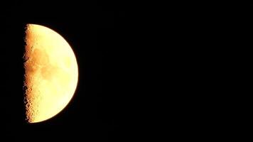 Timelapse. A glowing golden half moon as seen from earth through the atmosphere against a starry night sky. A large moon moves across the sky, the moon moving from the left frame to the right. video