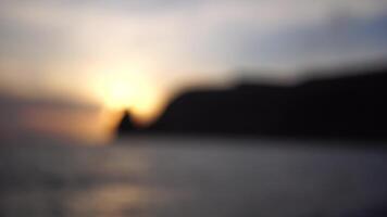 Sunset over the Scenic seascape with rocky shores silhoute. Small waves on golden warm water surface in motion blur with bokeh lights from sun. Holiday, vacation and recreational background concept video