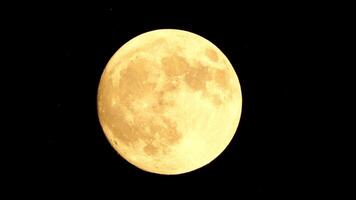 Glowing yellow huge full moon as seen from earth through the clouds against starry night sky. Large full moon moves across the sky, moon makes its way from bottom left frame to top right. video