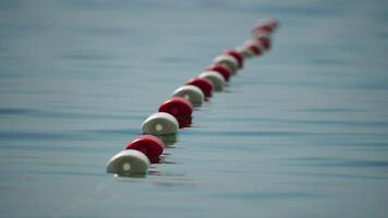 Orange and white safety buoys on a rope floating in the sea on a sunny day, close up. Fencing of the swimming area on the beach. Vacation, travel and holiday concept. Slow motion video