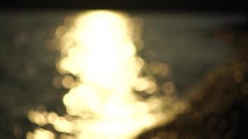 Blurred golden sea at sunset with shifting focus and bokeh effect. Sun reflects and sparkles on waves, illuminating golden sea. Holiday recreation concept. Abstract nautical summer ocean sunset nature video