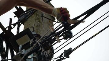 Skilled electrician fixes wires standing on ladder near high pole against blue sky on summer day backside view. Electrical service and mounting on the pole video