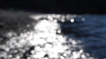 Abstract sea summer ocean sunset nature bokeh background. Small waves on azure water surface in motion blur with golden bokeh lights from sun. Holiday, vacation and recreational concept. Slow motion video