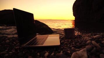 Silhouette of laptop and cup on the beach over sea sunset. Sparkling sea water on background. Freelancer, blogger working on notebook on the beach. video