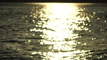 Blurred golden sea at sunset with shifting focus and bokeh effect. Sun reflects and sparkles on waves, illuminating golden sea. Holiday recreation concept. Abstract nautical summer ocean sunset nature video