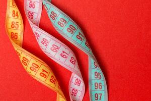 Close up of colorful measure tapes on red background. Perfect female figure measurements concept photo