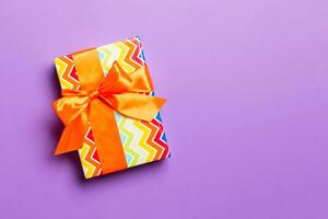 Gift box with orange bow for Christmas or New Year day on purple background, top view with copy space photo