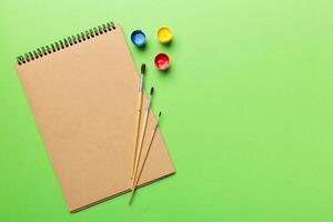 Album pages and paints, pencils, brush on a colored background. Top view with empty space. workplace for creativity. home teaching concept drawing photo