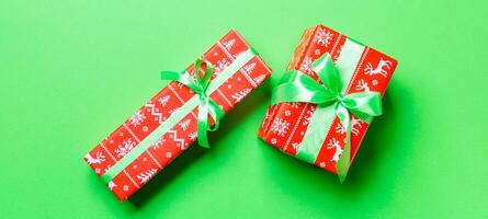 wrapped Christmas or other holiday handmade present in paper with green ribbon on green background. Present box, decoration of gift on colored table, top view photo
