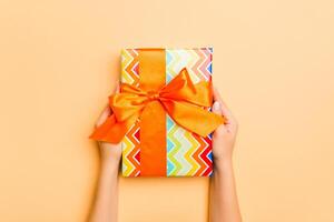 Flat lay of woman hands holding gift wrapped and decorated with bow on gold background with copy space. Christmas and holiday concept photo