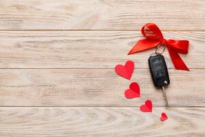 Car key with a red bow and a heart on Colored table. Giving present or gift for valentine day or christmas, Top view with copy space photo