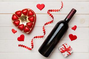 Bottle of red wine on colored background for Valentine Day with gift and chocolate. Heart shaped with gift box of chocolates top view with copy space photo