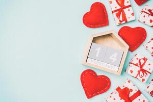 Holiday composition of gift boxes, wooden calendar and red textile hearts on colorful background with empty space for your design. The fourteenth of February. Top view of Valentine's Day concept photo
